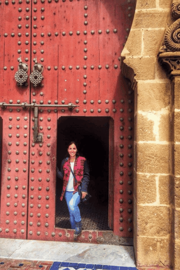 A woman standing in front of a red door in Meknes Morocco