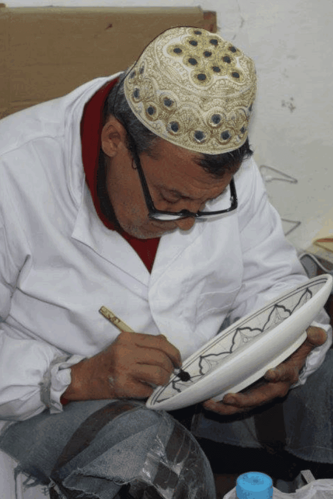 A man wearing a white shirt and a hat painting ceramic in Fez Morocco